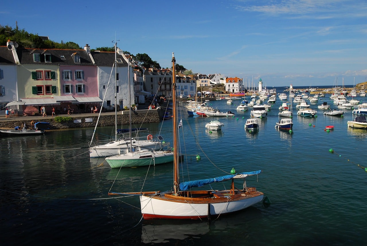 Port de Sauzon à Belle-Île-en-Mer, maisons pastel et bateaux amarrés se reflétant dans le calme de l’eau, sous une lumière d’été presque éternelle, aux portes de la côte sauvage — écrin d’un Divan double